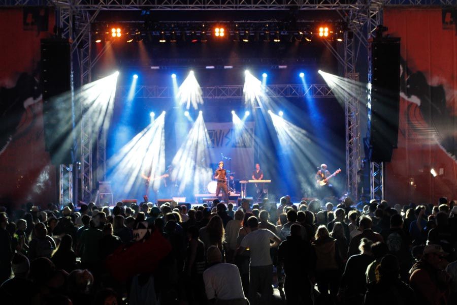 Open-Air-Bühne in blauem Licht mit Lichtkegeln, davor ein großes Publikum
