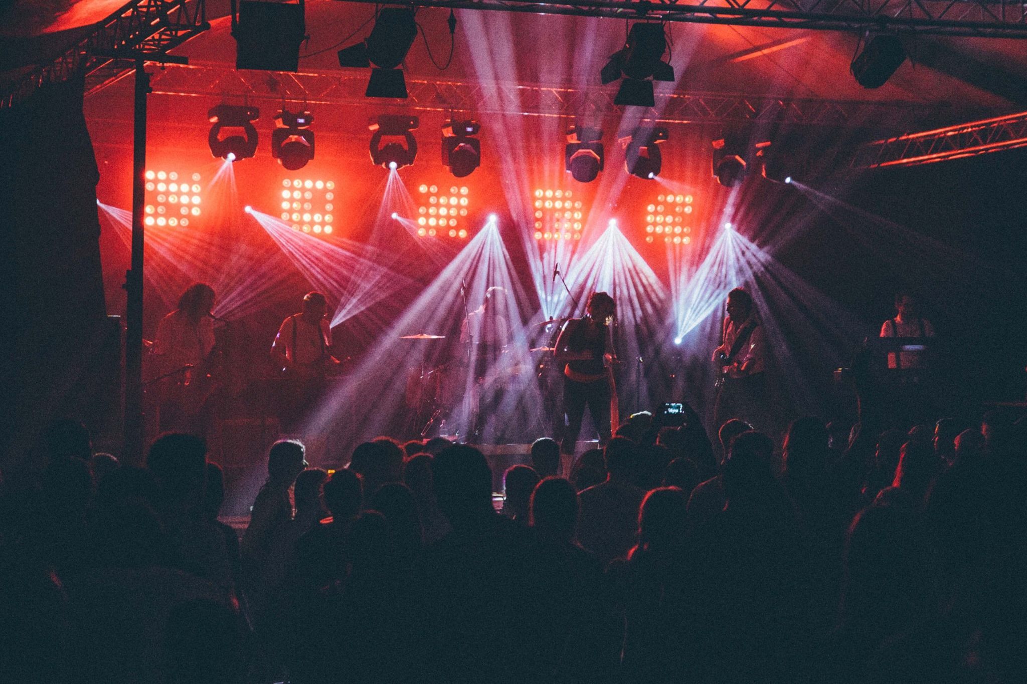 Band auf einer Bühne in rotem Licht mit Lichtkegeln über dem Publikum